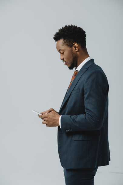 side view of african american man using smartphone isolated on grey  - Фото, изображение