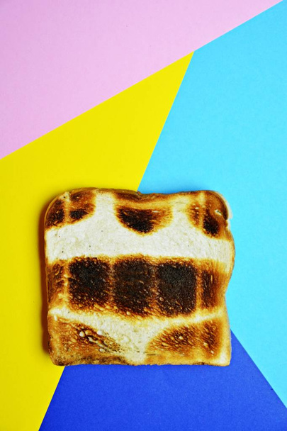 A toast lies on a colored surface. The toast is not toasted everywhere the same, but has not toasted parts in the form of a bikini - Abstract concept for sunburn in the summer  - 写真・画像