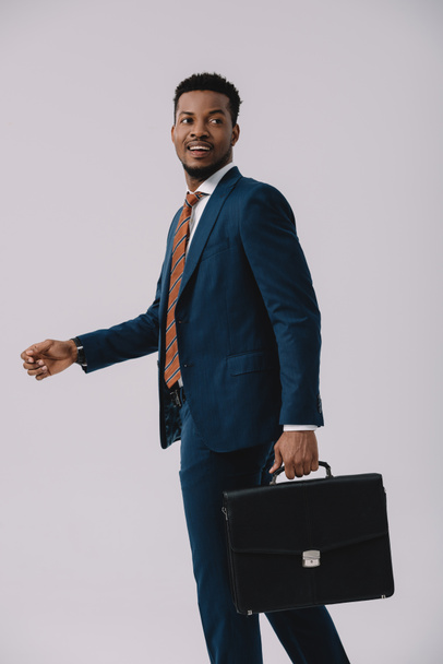 handsome african american man in suit holding briefcase isolated on grey  - Fotó, kép