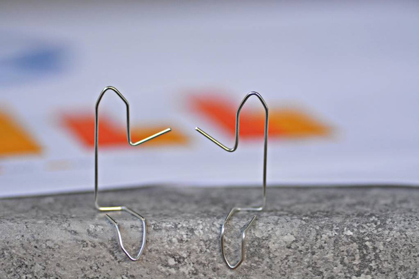 Two paperclips bent to small male sit on a surface and have statistical evaluations and diagrams behind them - Abstract concept for representing business discussions  - Photo, Image