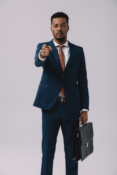 selective focus of african american man pointing with finger while holding briefcase isolated on grey  - Foto, Bild