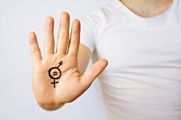 Parikymppinen mies on maalannut käteensä merkin sukupuolten tasa-arvosta ja näyttää sen kameralle - käsitteen miesten ja naisten tasa-arvon vaatimisesta
  - Valokuva, kuva