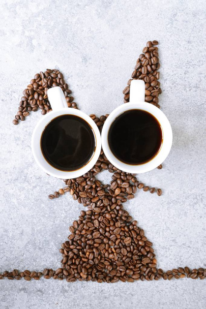 新鮮なコーヒー豆と淹れたてのブラックコーヒーのカップ2杯で、ウサギは明るい大理石の表面に形を整え、イースターの贈り物としてコーヒー豆をコンセプトにしています。  - 写真・画像
