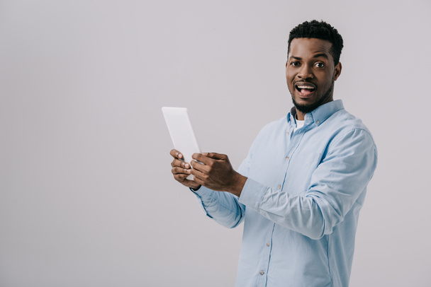excited african american man holding digital tablet  isolated on grey  - Φωτογραφία, εικόνα