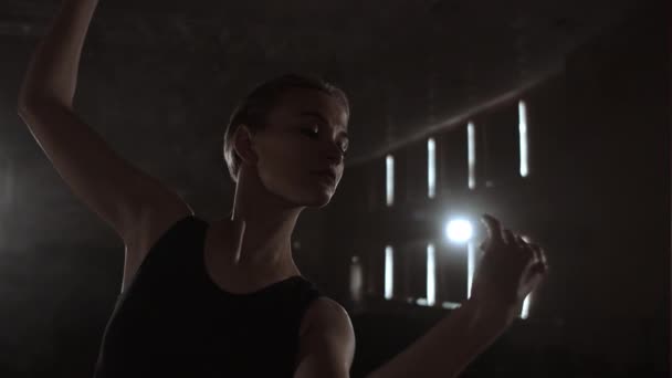 Close-up of ballet dancer as she practices exercises on dark stage or studio. Ballerina shows classic ballet pas. Slow motion. Flare, gimbal shot - Záběry, video