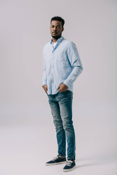 handsome african american man standing with hands in pockets on grey  - Photo, image