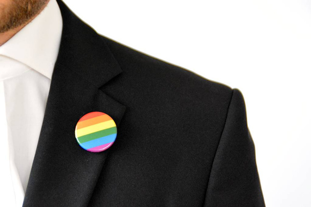 Ένας άντρας στα τριάντα του φοράει ένα κουμπί με το σύμβολο του τρανσέξουαλ στο σακάκι του-ιδέα για αποδοχή και ανοχή στην εργασία - Φωτογραφία, εικόνα