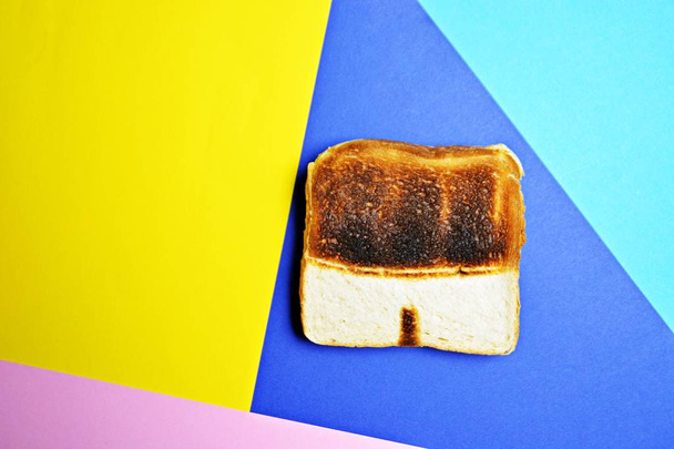 A toast lies on a colored surface. The toast is not toasted the same everywhere, it has untoasted spots that form the shape of a swimming trunks - Abstract concept for sunburn in the summer  - Foto, Bild