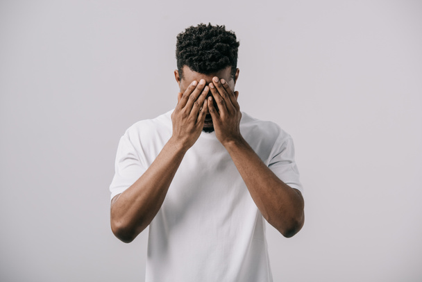 hombre afroamericano en camiseta blanca que cubre la cara con las manos aisladas en gris
  - Foto, Imagen