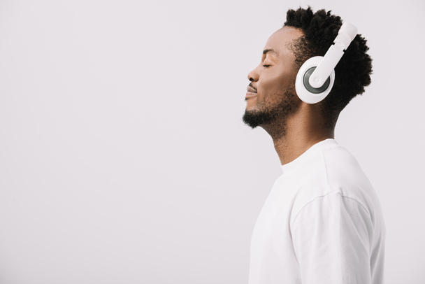 白のヘッドフォンで音楽を聴く幸せなアフリカ系アメリカ人男性の側面図  - 写真・画像