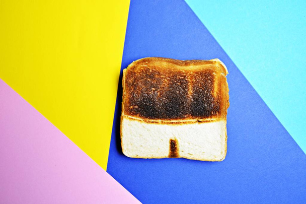 A toast lies on a colored surface. The toast is not toasted the same everywhere, it has untoasted spots that form the shape of a swimming trunks - Abstract concept for sunburn in the summer  - Foto, Imagem