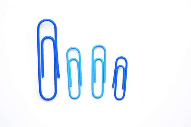 Verschillende grote blauwe paperclips liggen naast elkaar op een wit oppervlak  - Foto, afbeelding
