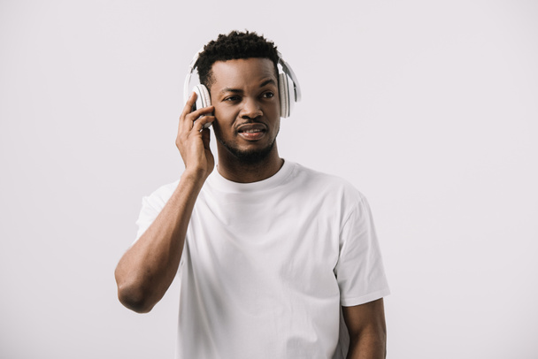 白で隔離されたヘッドフォンに触れながら音楽を聴いているアフリカ系アメリカ人男性  - 写真・画像