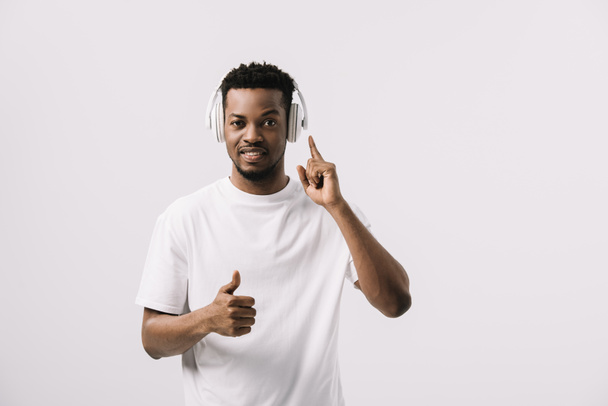 guapo afroamericano hombre escuchando música y mostrando el pulgar hacia arriba aislado en blanco
  - Foto, imagen