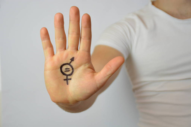A man in his mid-twenties has painted a sign of gender equality on his hand and shows it to the camera - a concept for demanding equality between men and women  - Photo, Image
