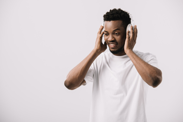 hombre afroamericano feliz sonriendo y tocando auriculares en blanco
  - Foto, Imagen