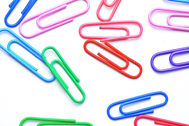 Various colored paper clips lie across a white surface - a background consisting of a white base and colorful paperclips - Photo, Image