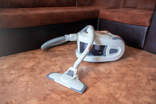 The big white vacuum cleaner with the water filter costs in the apartment on a floor against the background of a brown sofa - Photo, Image