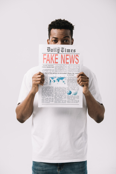 hombre afroamericano rizado cubriendo la cara mientras sostiene el periódico con letras de noticias falsas aisladas en blanco
  - Foto, imagen