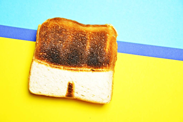 A toast lies on a colored surface. The toast is not toasted the same everywhere, it has untoasted spots that form the shape of a swimming trunks - Abstract concept for sunburn in the summer  - Photo, Image
