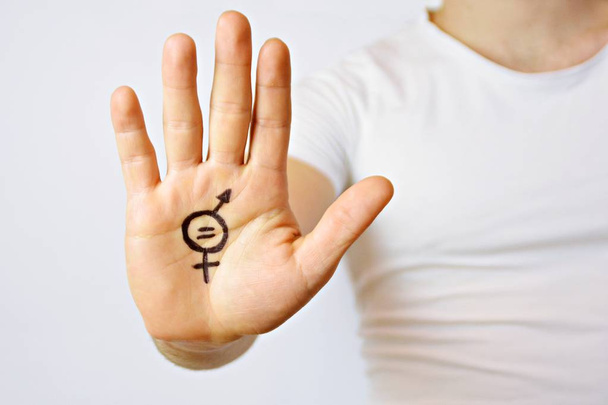 ein Mann Mitte Zwanzig hat sich ein Zeichen der Gleichberechtigung der Geschlechter auf die Hand gemalt und zeigt es der Kamera - ein Konzept zur Forderung nach Gleichberechtigung von Männern und Frauen  - Foto, Bild