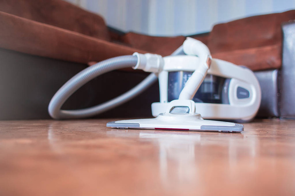 Le grand aspirateur blanc avec le filtre à eau coûte dans l'appartement sur un sol sur le fond d'un canapé brun
 - Photo, image