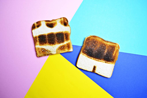 Three toasts lie on a colorful background - these are not toasted on the whole surface but show the contours of trunks and bikini and those of a sun - concept of sunburn presented with toasts  - Photo, Image