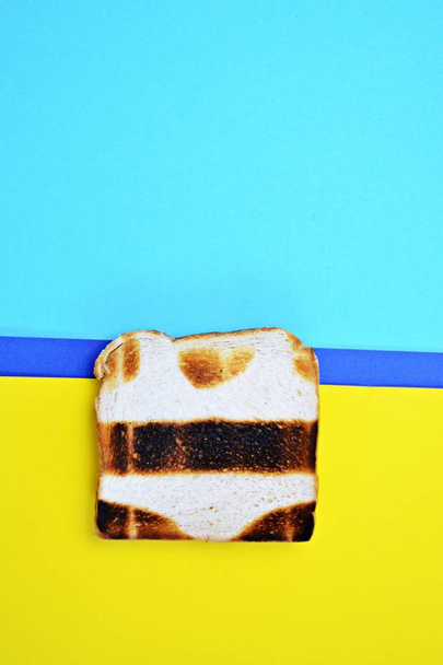 A toast lies on a colored surface. The toast is not exactly toasted everywhere, but has not toasted parts in the form of a bikini - Abstract concept for sunburn in the summer - Photo, Image