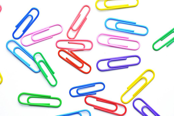 Various colored paper clips lie across a white surface - a background consisting of a white base and colorful paperclips - Photo, Image