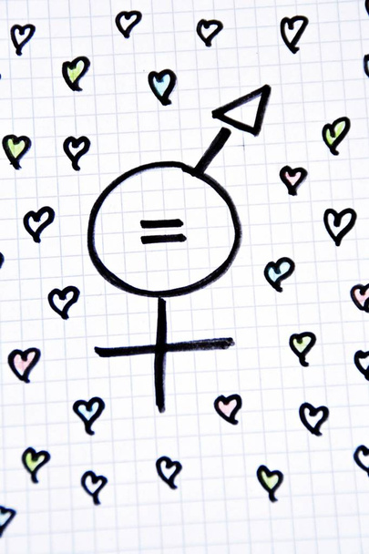 A sign for the equality of man and woman consisting of the respective gender signs and a same with partly painted hearts on a drawn sheet drawn - equality man and woman symbolically represented  - Photo, Image