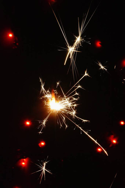Wunderkerze in der Nacht vor bunten Lichtern - in der Silvesternacht brennt eine Wunderkerze langsam ab und funkt in alle Richtungen  - Foto, Bild