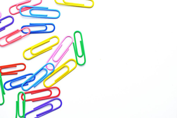 Various colored paper clips lie across a white surface - a background consisting of a white base and colorful paperclips - Photo, image