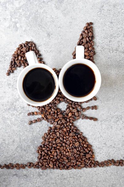 新鮮なコーヒー豆と淹れたてのブラックコーヒーのカップ2杯で、ウサギは明るい大理石の表面に形を整え、イースターの贈り物としてコーヒー豆をコンセプトにしています。  - 写真・画像