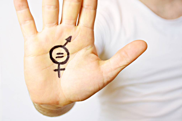 ein Mann Mitte Zwanzig hat sich ein Zeichen der Gleichberechtigung der Geschlechter auf die Hand gemalt und zeigt es der Kamera - ein Konzept zur Forderung nach Gleichberechtigung von Männern und Frauen - Foto, Bild