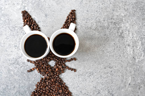 Со свежими кофейными зернами и двумя чашками свежеваренного черного кофе, заяц имеет форму на яркой мраморной поверхности - концепция с кофейными зернами в качестве подарка на Пасху - с местом для текста или других элементов
  - Фото, изображение