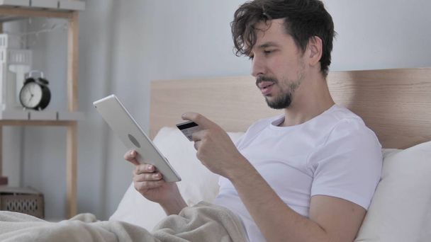Online-Shopping auf dem Tablet von jungem Mann im Bett - Foto, Bild