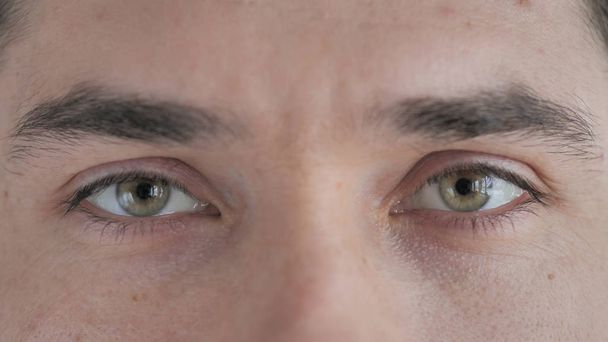 close-up van knipperende ogen van jonge man kijken naar camera - Foto, afbeelding