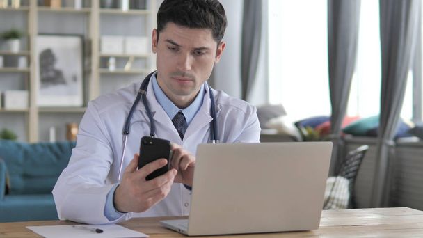 Médico trabalhando no laptop e usando Smartphone
 - Foto, Imagem