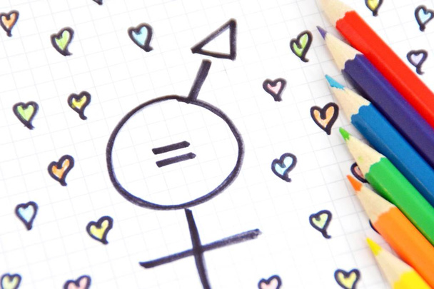 Un signo para la igualdad del hombre y la mujer que consiste en los respectivos signos de género y una coincidencia con corazones pintados y lápices de colores en una hoja dibujada igualdad hombre y mujer representados simbólicamente
 - Foto, Imagen