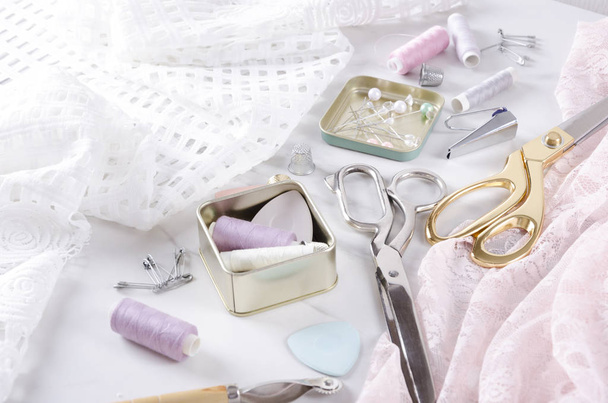 Boxes with thread, pins, golden and silver scissors, elegant fabric on the white table.Sewing process.Closeup of sewing tools - Photo, Image