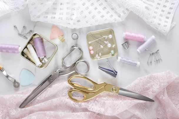 Tela rosa y blanca, tijeras doradas y plateadas, carretes de hilo y diferentes herramientas de costura profesionales, vista superior
 - Foto, imagen
