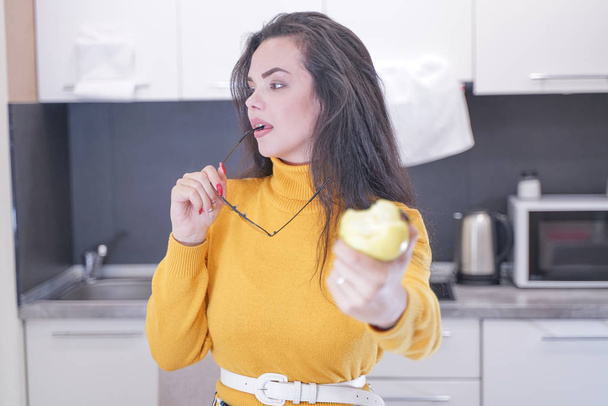 白いキッチンの背景にリンゴを噛む素敵なかわいい女の子のクローズアップポートレート - 写真・画像