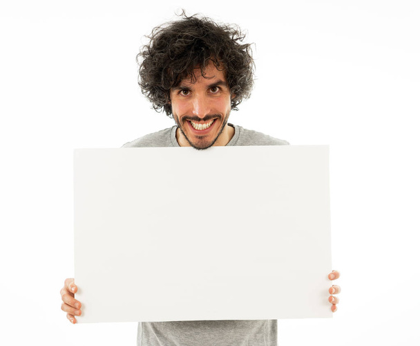Funny and good looking millennial man showing and pointing at blank board with copy space for text. Friendly and excited young stylish man holding blank poster for advertisement. In marketing concept. - Foto, Imagen