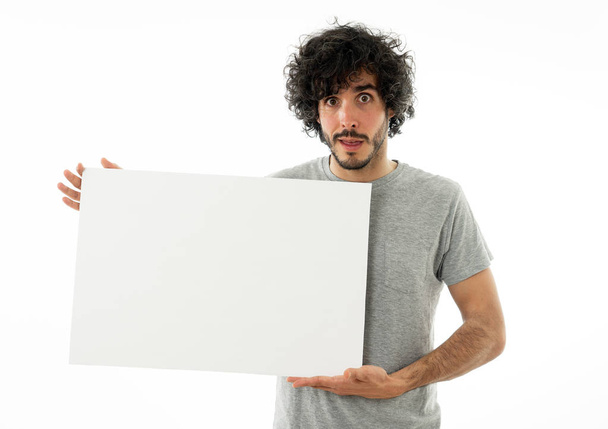 Funny and good looking millennial man showing and pointing at blank board with copy space for advertisement text. Looking happy surprised and shocked at great ad. In marketing concept. - Foto, Imagen