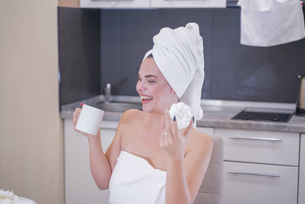 jeune fille assise dans la cuisine après une douche enveloppée dans une serviette blanche et se reposant
 - Photo, image