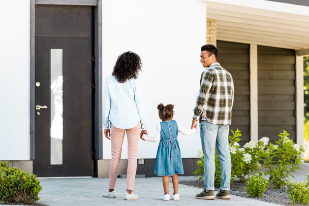 full length view of african american family standing near new house while parents holding hands with kid - Foto, afbeelding