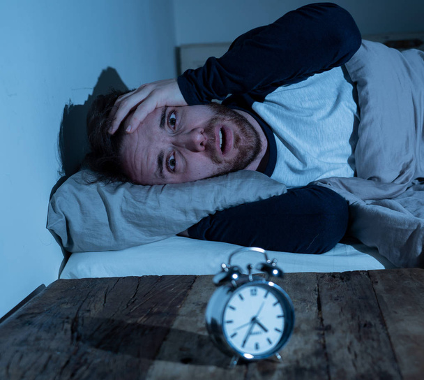 Schlaflosigkeit Stress und Schlafstörungen Konzept. schlaflose verzweifelte junge kaukasische Mann wach in der Nacht nicht in der Lage zu schlafen, fühlen sich frustriert und besorgt aussehen gestresst und besorgt am Wecker. - Foto, Bild