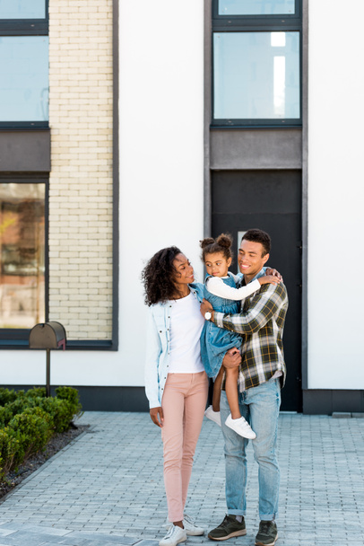 vista completa della famiglia afro-americana in piedi vicino alla nuova casa mentre il padre tiene il bambino e la madre a guardare il bambino
 - Foto, immagini