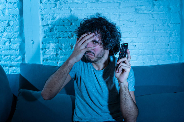 Lifestyle portrait of young man feeling scared and shocked making fear, anxiety gestures while watching television holding remote control. In horror and violence on TV and internet and mass media. - Fotoğraf, Görsel