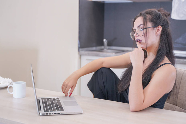 aranyos lány szemüveg ül az asztalnál egy laptop otthon egyedül - Fotó, kép